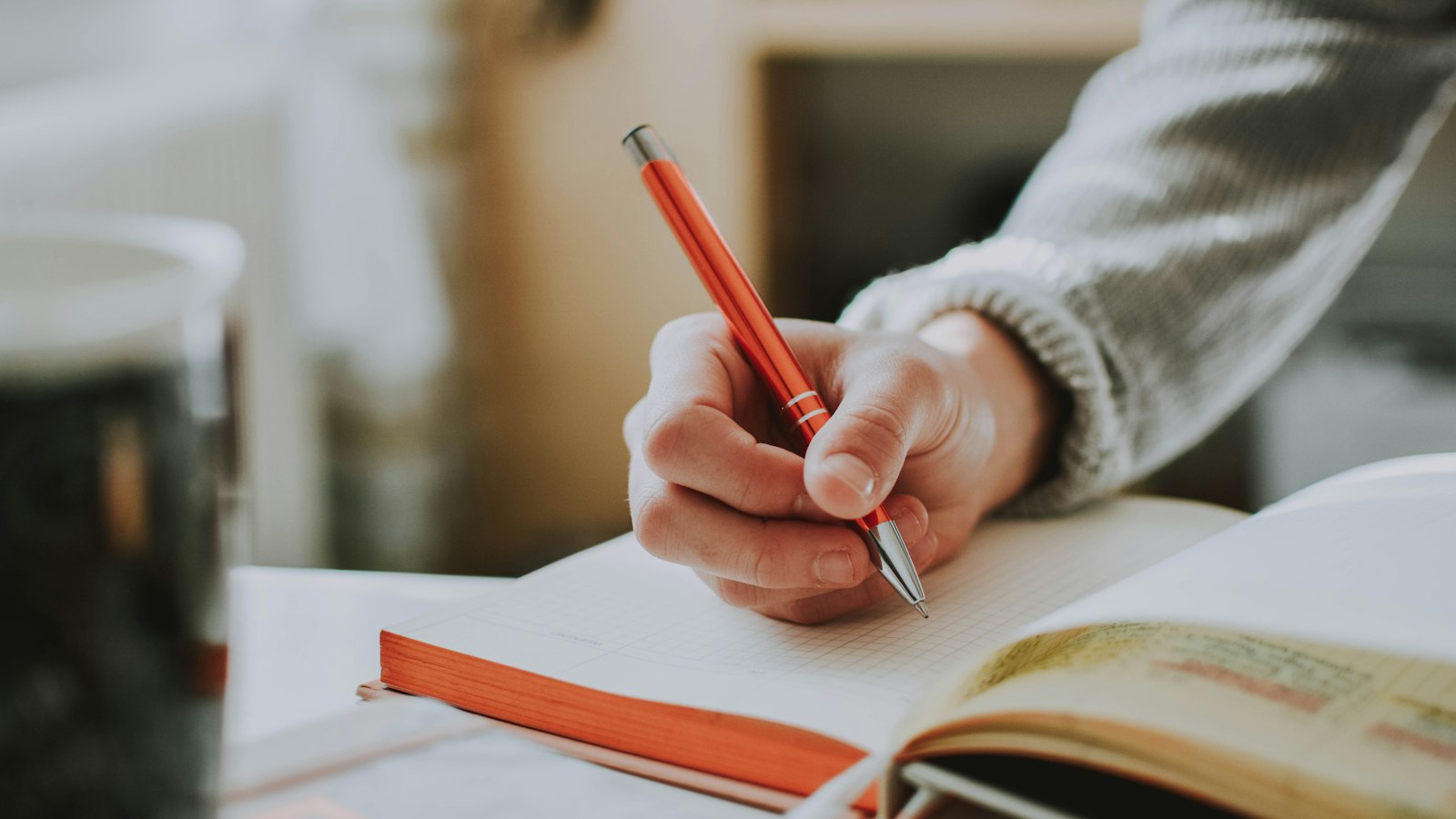 Person writing in a notebook with a red pen